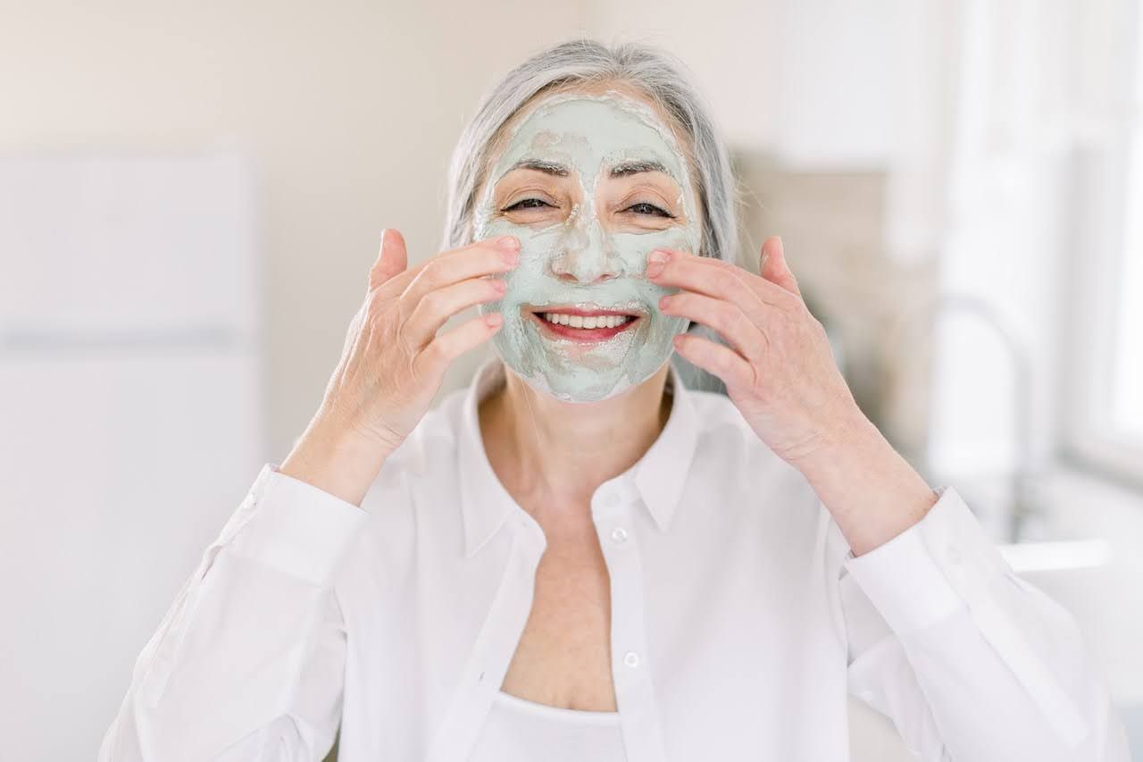 Smiling senior woman applying a calming face masque at home