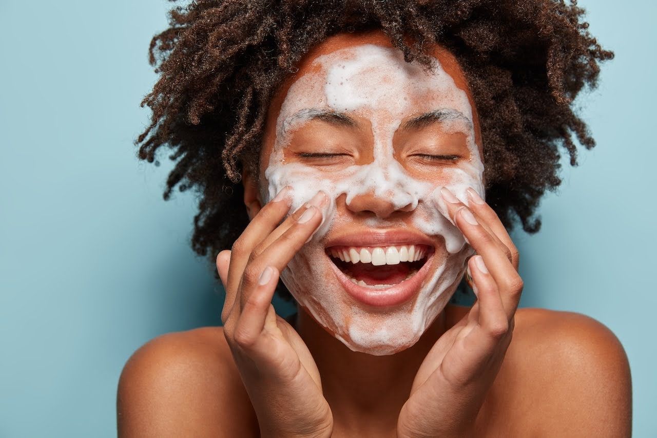 Smiling woman washing face as part of hyperpigmentation treatment routine