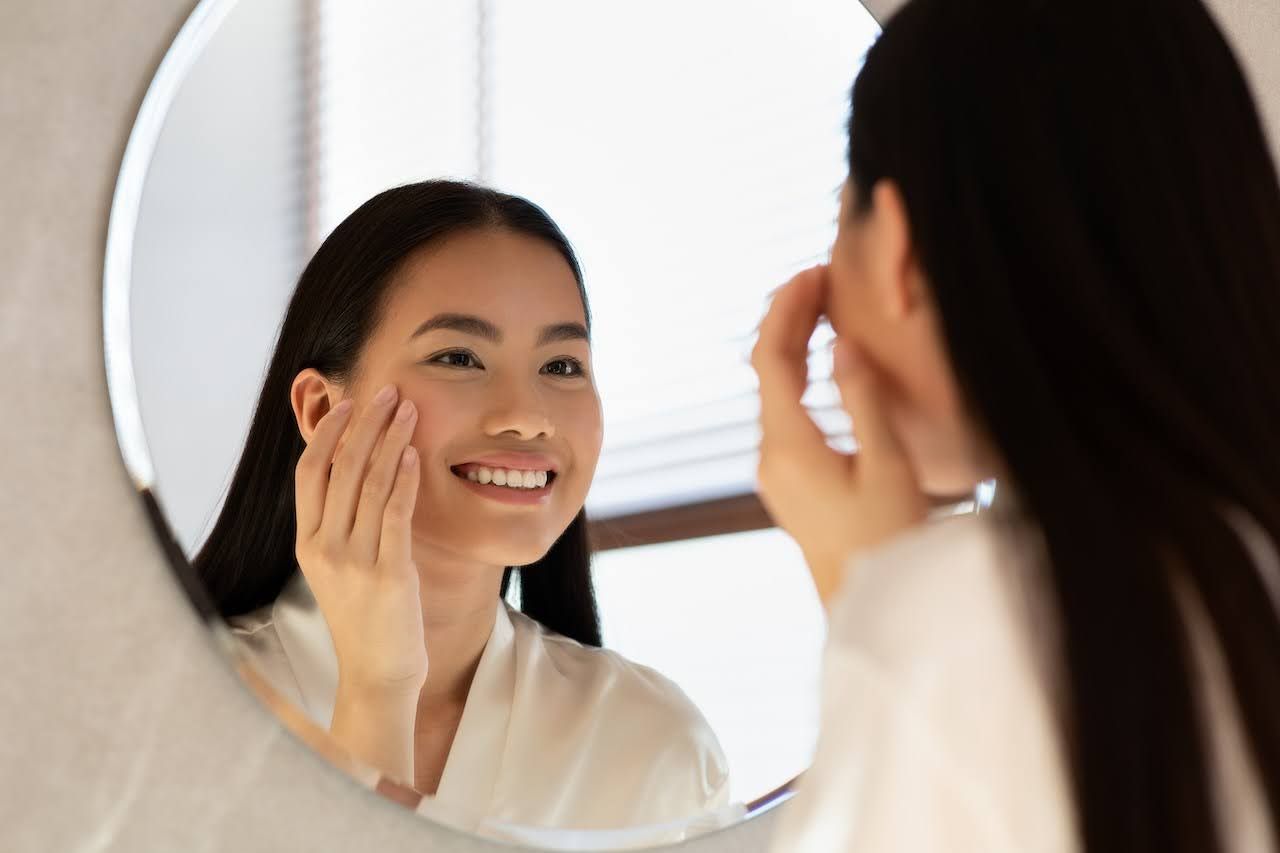 Woman looking in mirror after using skin brightening products