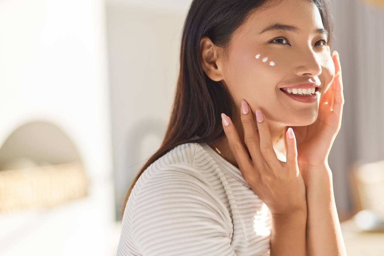 Woman with healthy skin applying moisturizer to face