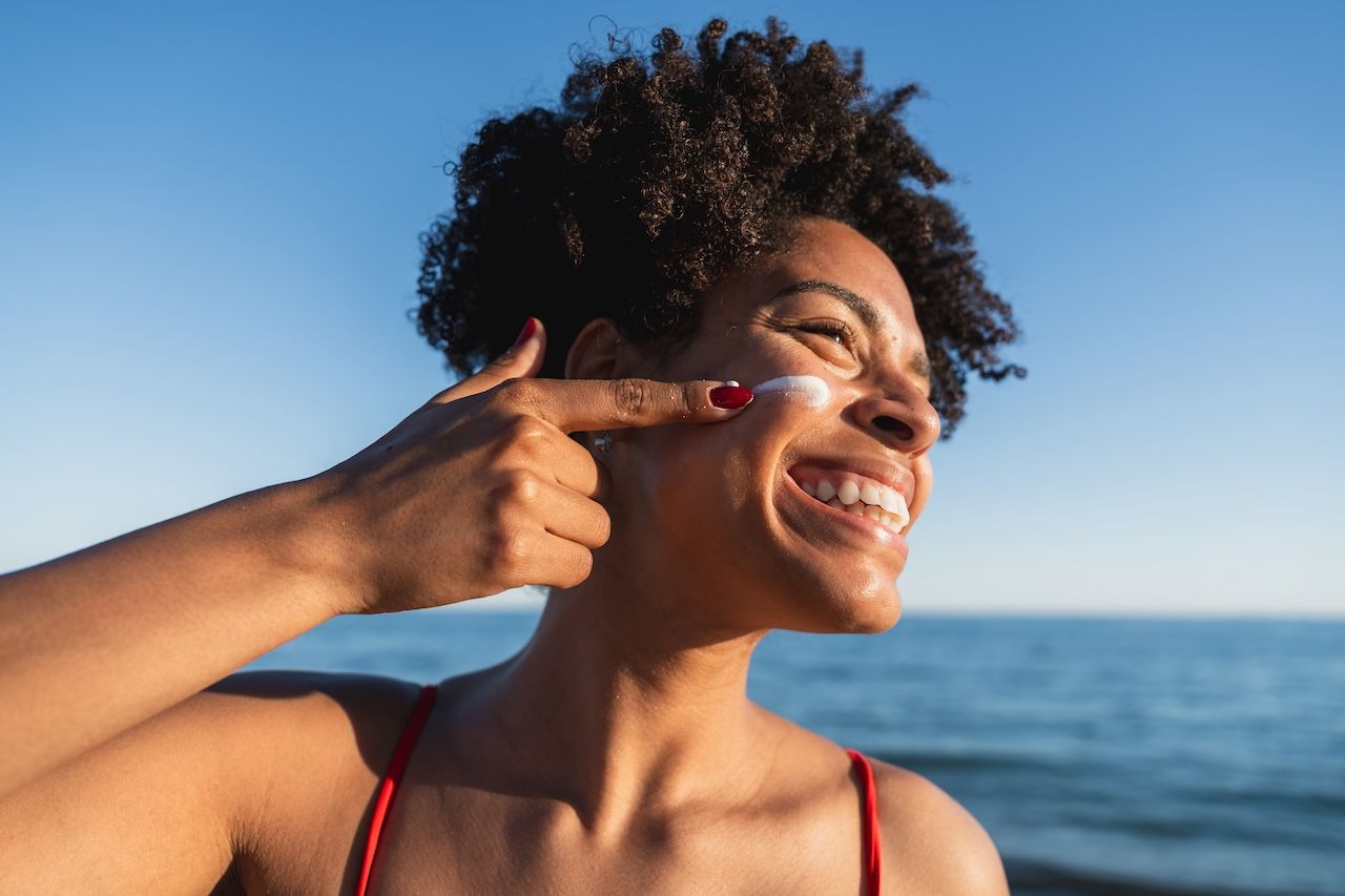 woman applying sunscreen outdoors to help protect skin from UV related aging